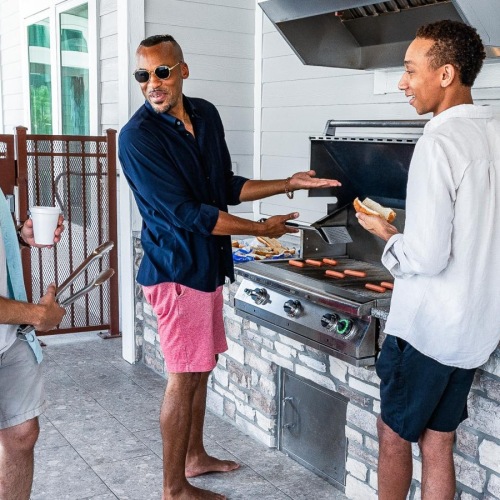 a group of men standing around a grill with food